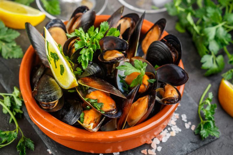 An orange bowl with mussels and parsley, where the orange from the mussels can be clearly seen