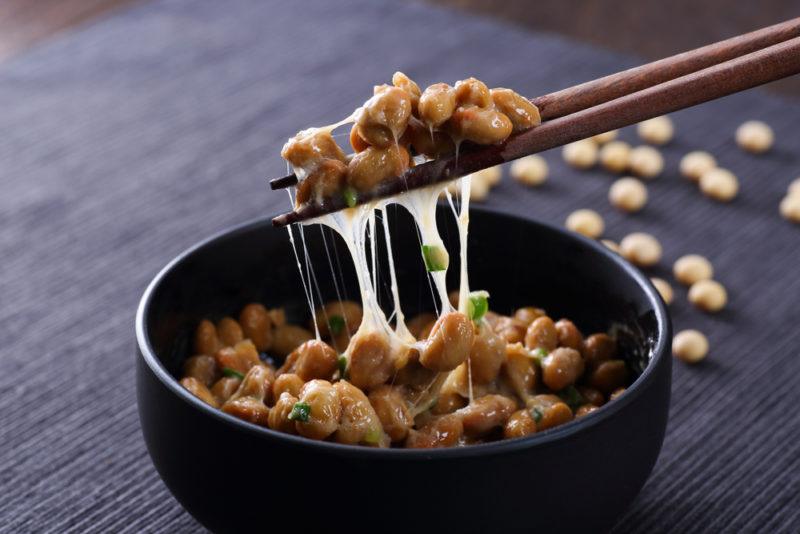 A black bown containing natto with chopsticks