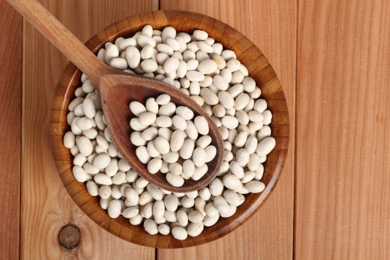 A brown bowl with navy beans and a spon with the beans