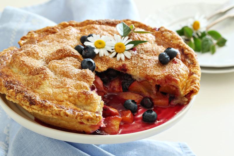 A white dish a nectarine and blueberry pie on a blue cloth