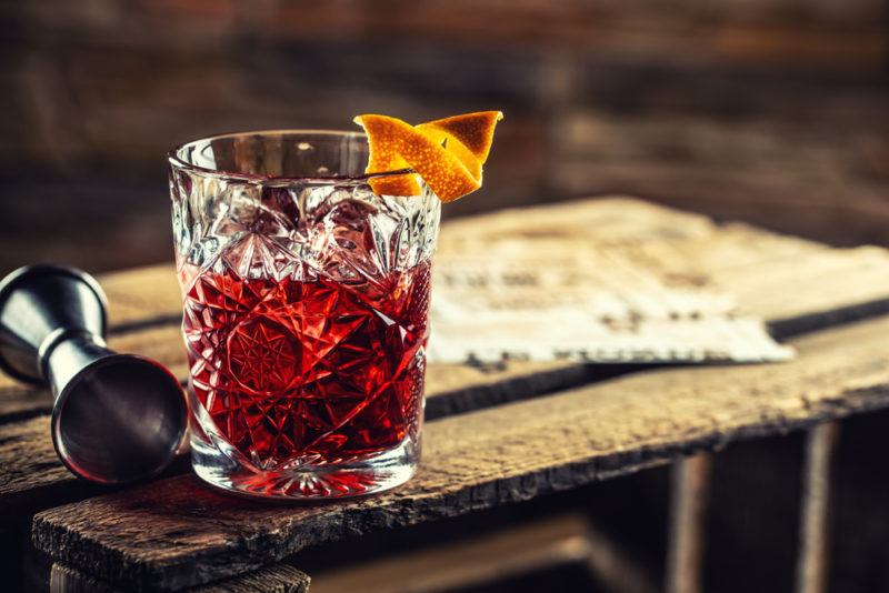 A Negroni cocktail on a bench with a measure and a twist