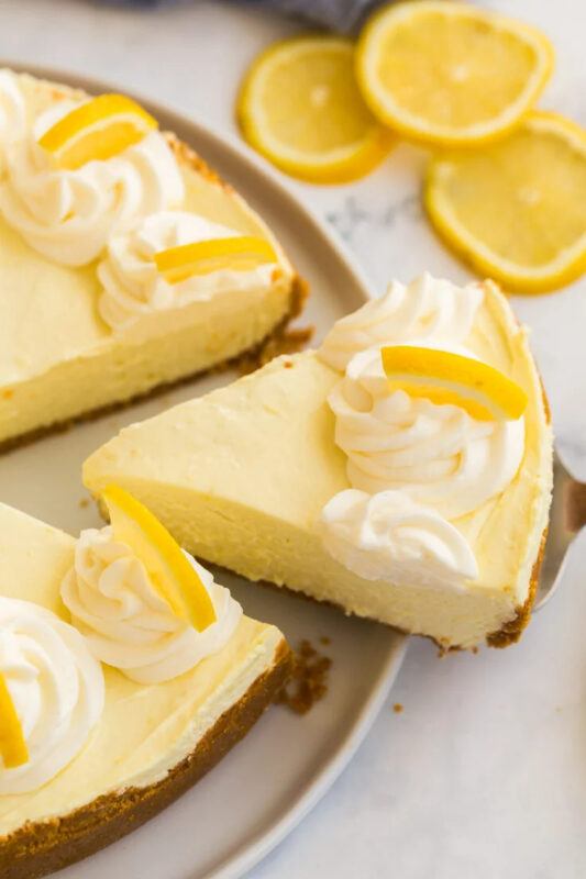 A pan containing a no bake lemon cheesecake topped with cream and lemons, from Recipe Rebel