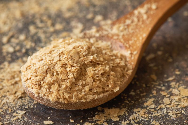 A wooden spoon with nutritional yeast and more yeast scattered on the table