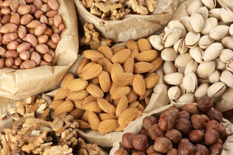 This photo shows an overhead view of several types of nuts in brown paper bags.