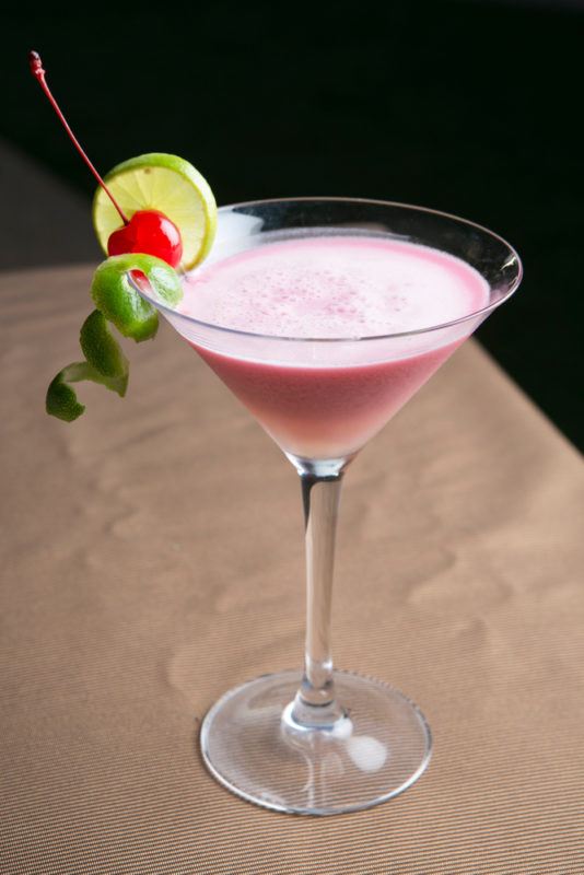 A martini glass with a pink nuts and berries cocktail