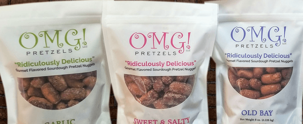 Three bags of OMG! Pretzels, white bags with different colored font depending on the variety.  Featured in the photo are garlic, sweet and salty, and old bay