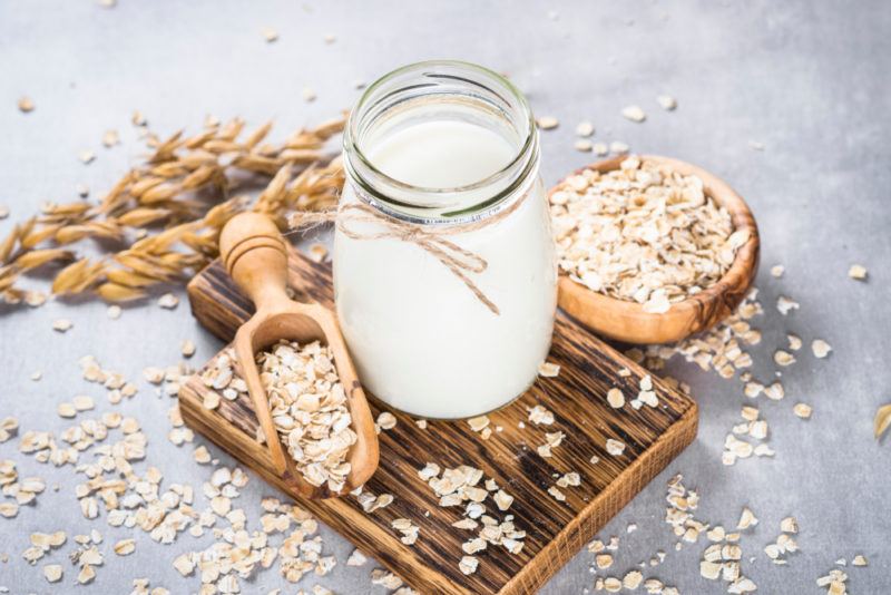 A glass jar of oat milk, with a bowl of oats and a spoon of oats