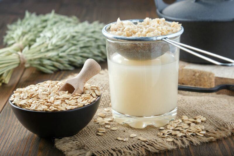 Oat milk being made at home with a strainer, next to a bowl of oats