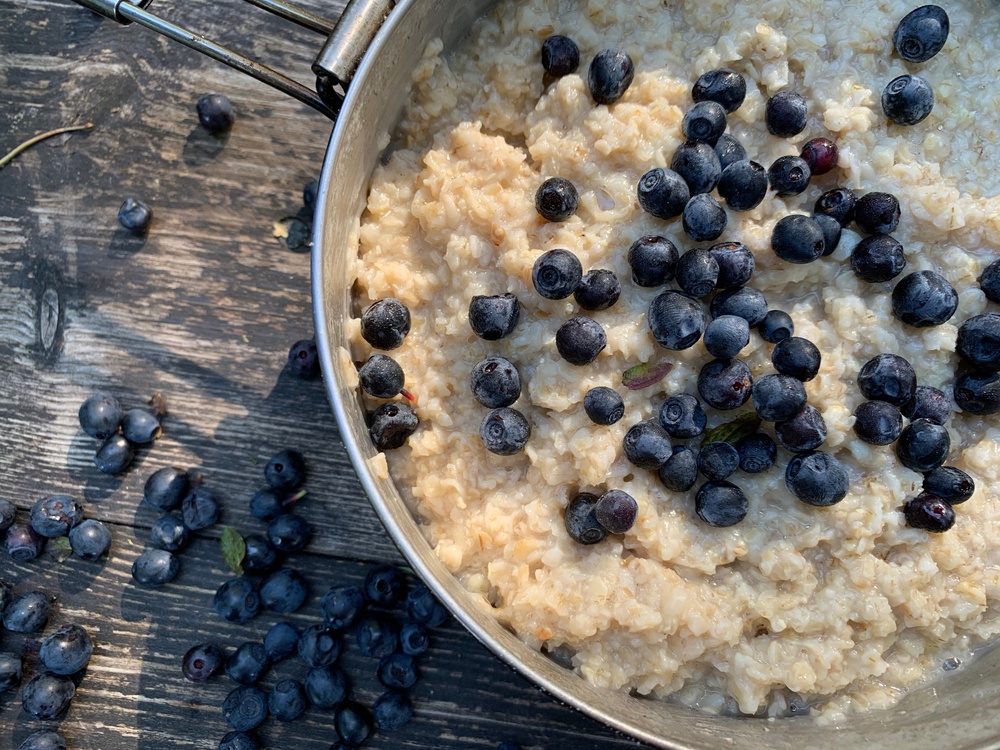 A pot of oatmeal with blueberries, with more blueberries scattered on the table