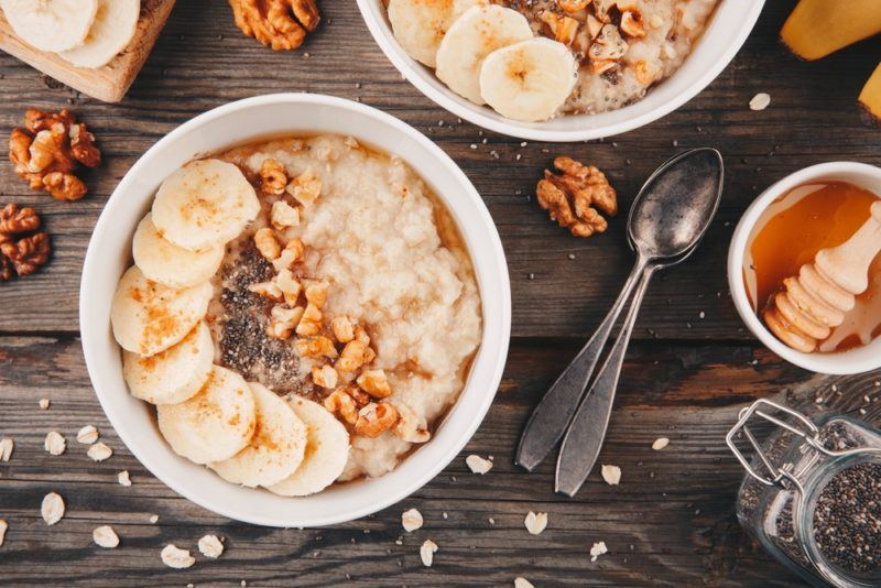 Two white bowls that contain oatmeal, sliced bananas and nuts