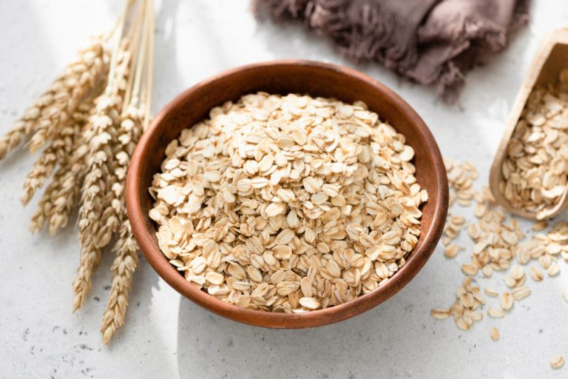 A wooden bown containing oats next to heads of grain