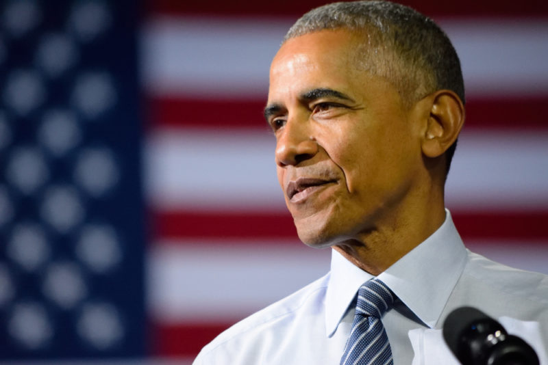 Obama standing in front of an American flag while wearing a dress shirt and a tie