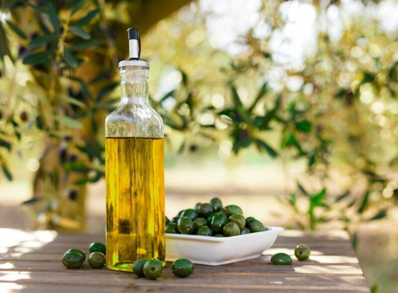 A bottle of fresh olive oil outside next to bowls of olives