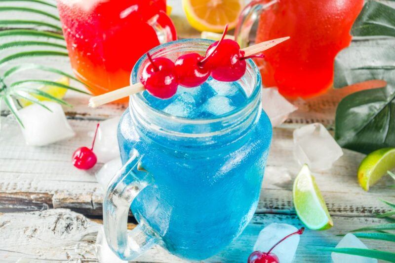 A mason jar containing a blue breeze cocktail, next to two red cocktails