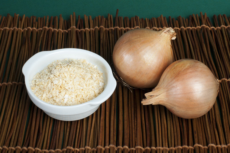 a small white bowl with onion powder, resting on a bamboo placemat with two fresh onion beside it.