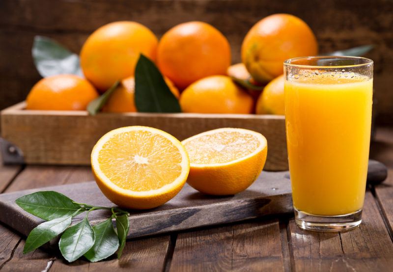 A glass of orange juice, a sliced orange and a box full of oranges