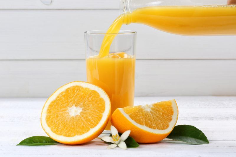 Orange juice being poured into a glass with oranges