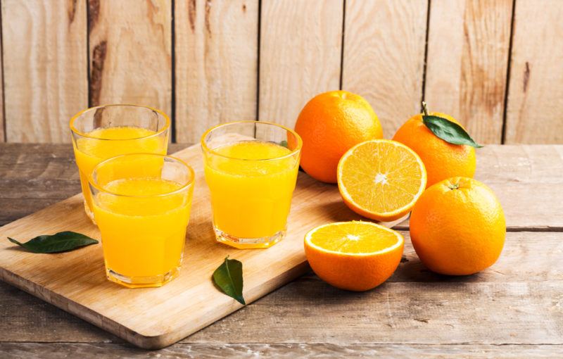 A cutting board with glasses of orange juice, along with oranges and a sliced orange