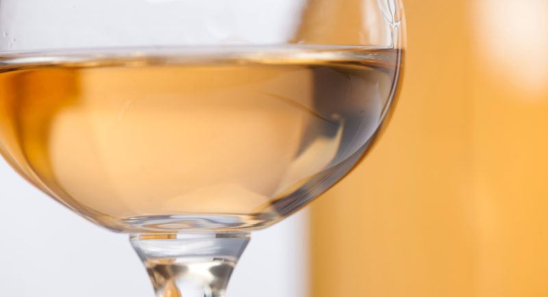 A glass of orange muscat wine with a bottle out-of-focus in the background