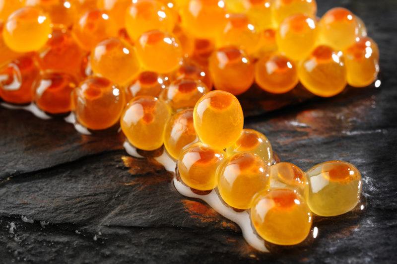 A macro image of orange fish eggs on a black surface