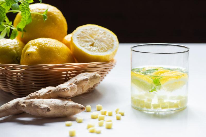 A glass of homemade lemonade, next to a basket of lemons and some ginger