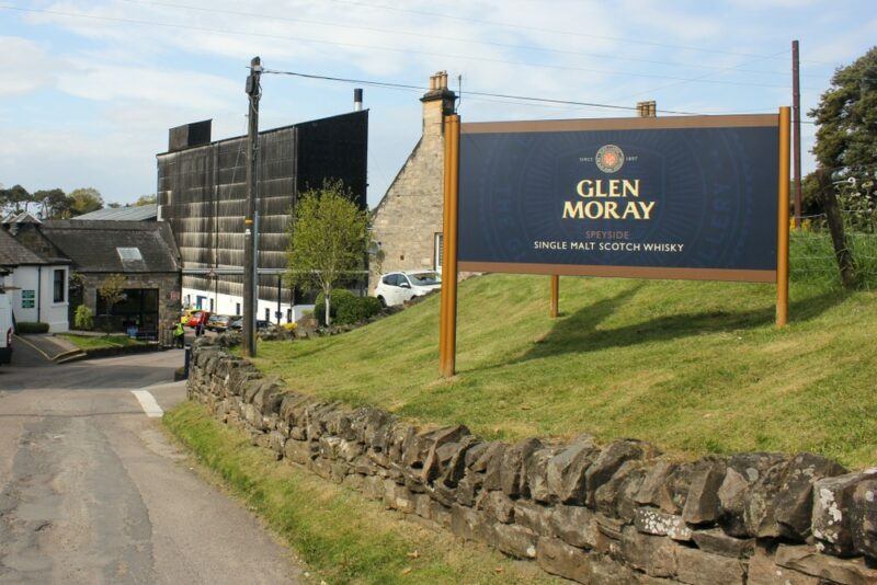 A town in Scotland, showing a sign for Glen Moray whisky, with the distillery in the background