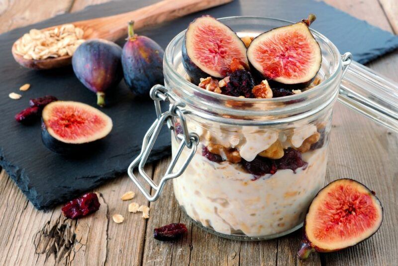 A single jar containing overnight oats, topped with figs and some other ingredients. There are also some figs on the table and a wooden spoon in the background