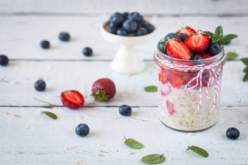 A jar of overnight oats that uses various types of berries, along with berries on a wooden table