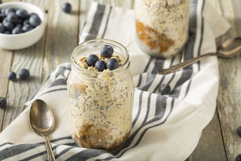 Two jars containing overnight oats, chia seeds, nut butter and blueberries