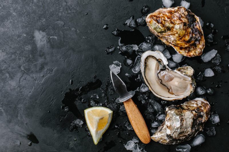 A black table with fresh ice, lemon wedges, and a shucking tool