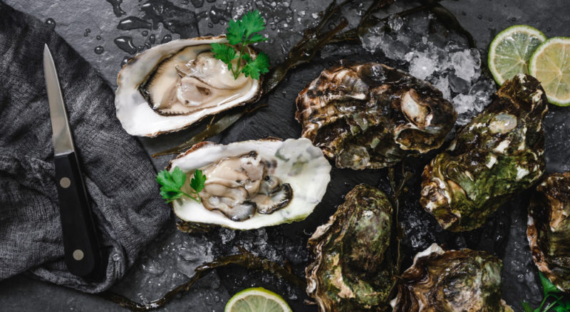 A selection of oysters on a black board with a knife and lime slices