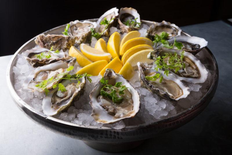 A black bowl with oysters and sliced lemons on a bed of rice