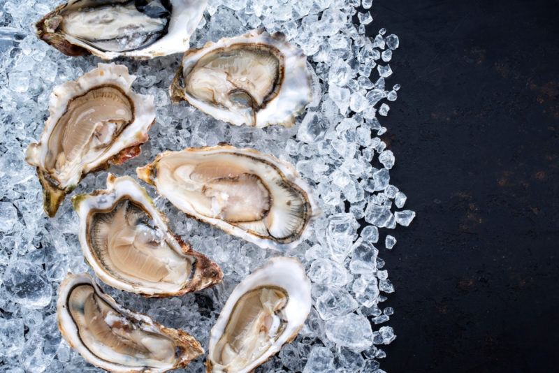 A selection of fresh oysters laying open on ice against a black background