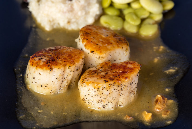 Three pan fried scallops in juice, next to potatoes and lima beans