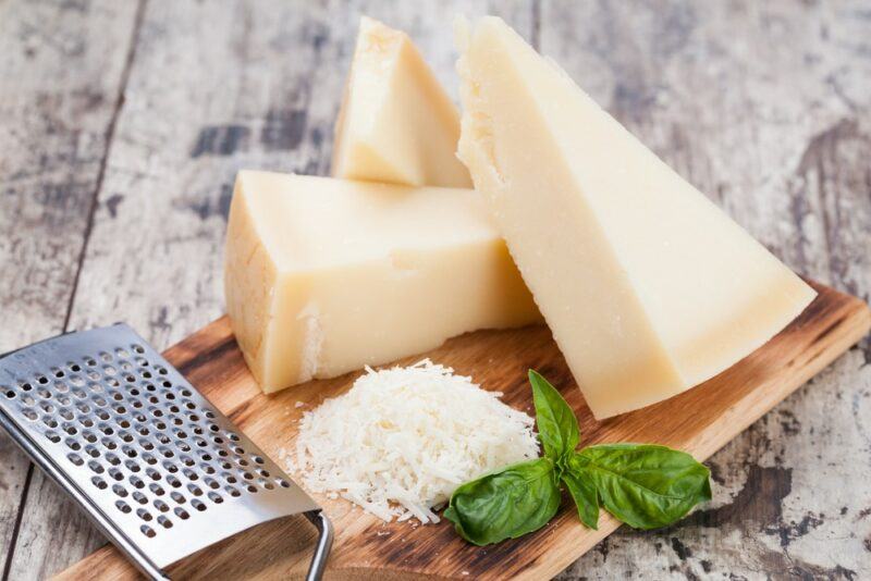 A wooden tray with parmesan wedges, a grater, and some grated parmesan