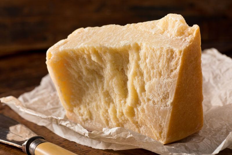 A wooden board with a wedge of parmesan cheese on paper