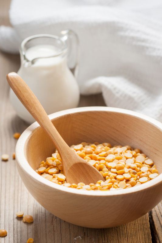 A bowl of yellow split peas in front of a glass jug of pea milk