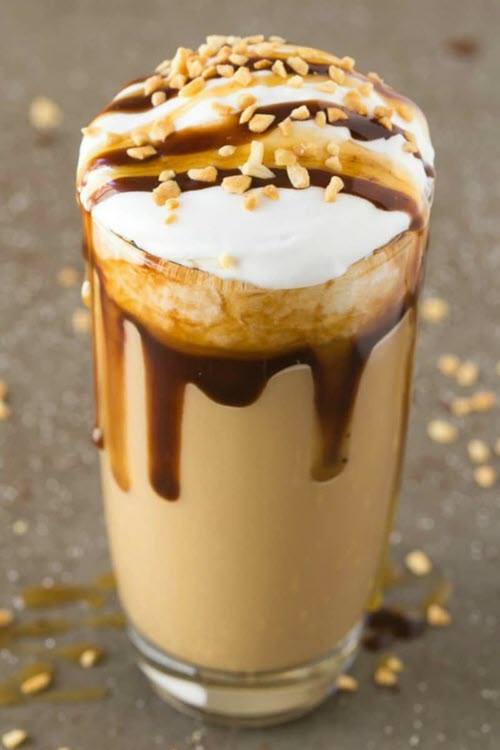 A tall glass containing a peanut butter smoothie with cream on top and peanut butter plus sauce running down the sides