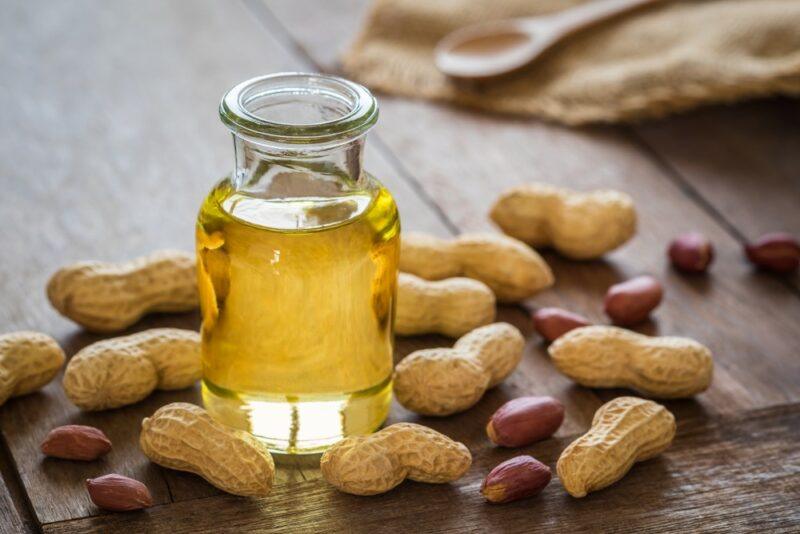 A wooden table with peanuts, some in their shells and a few not, plus a glass bottle of peanut oil