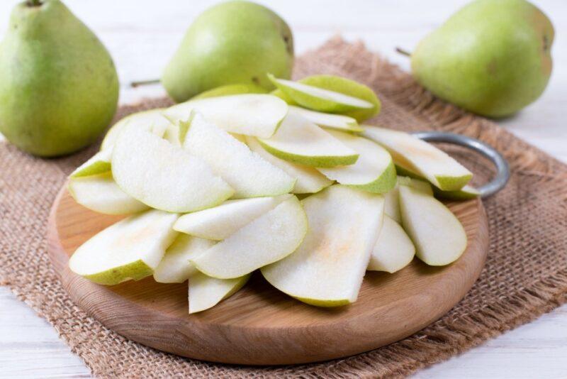 A circular wooden board with sliced pears, with three pears in the background