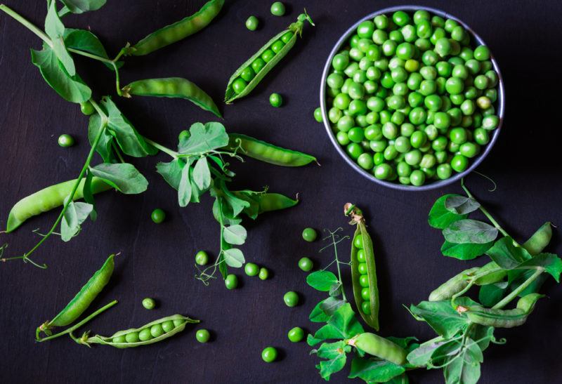 A bowl of peas with unshelled peas scattered across the table