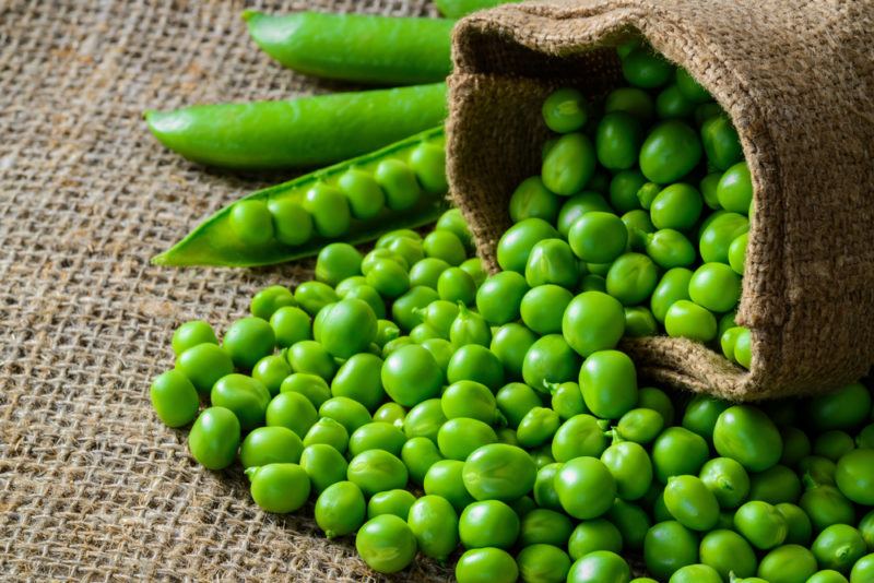 A bag of fresh peas spilling out onto the table