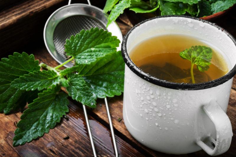 A white mug of peppermint tea with peppermint leaves and a strainer