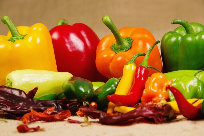 Several types of peppers in yellow, red, orange, and green colors rest against a beige background.