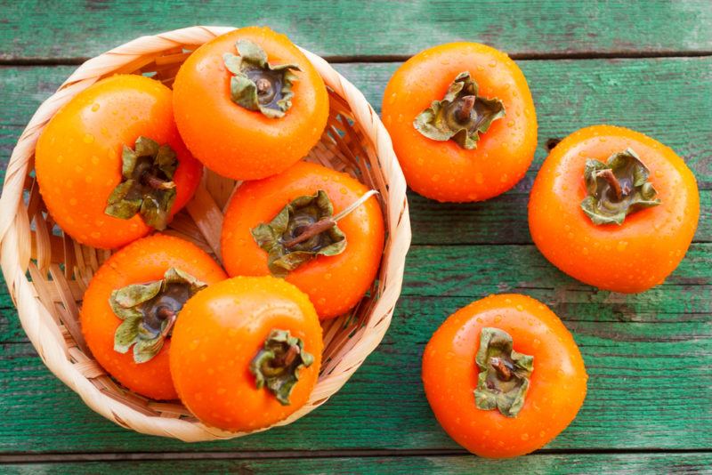 A wicker basket of fresh persimmons with a few on a table