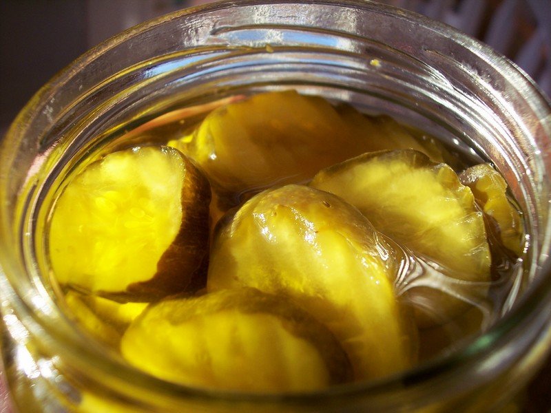 This photo shows a closeup of the top of an open jar of pickled cucumber slices.