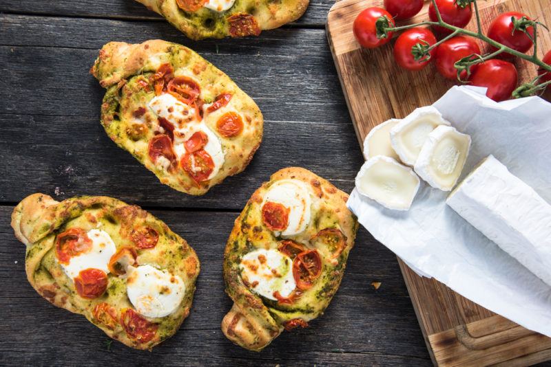 Three pieces of picnic bread with eggs next to a wooden board with tomatoes and cheese