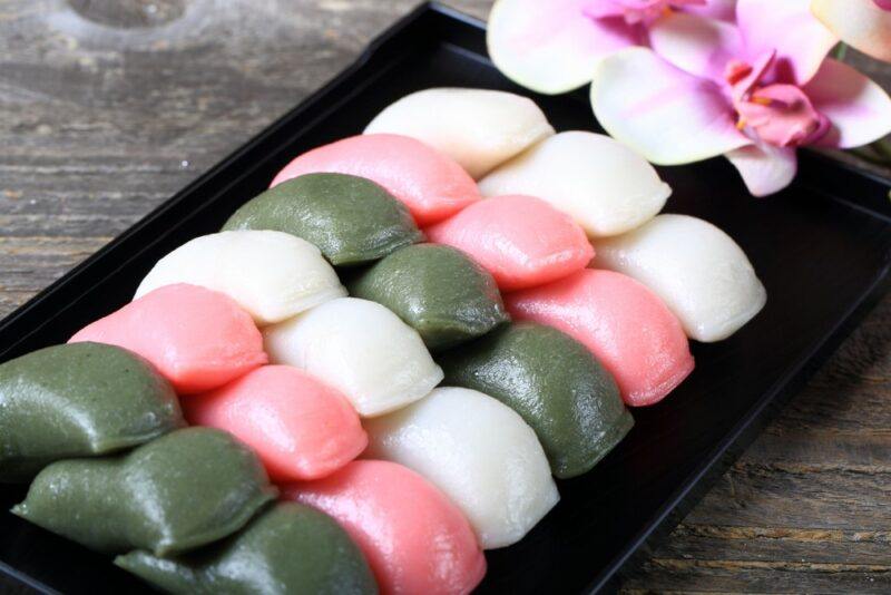 A black dish with green, pink, and white rice cakes arranged in lines