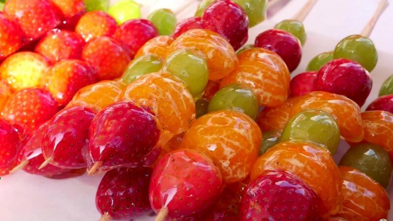 A white plate with skewers of candied fruit, part of a treat called tanghulu