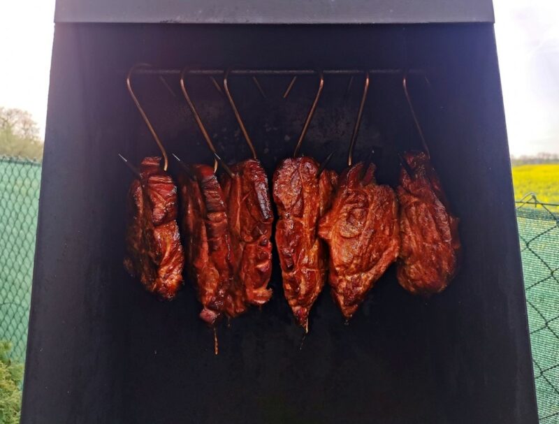 Pieces of meat hanging in a smoker | Food For Net The interior of a propane smoker with hanging pieces of meat